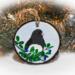 A dark-eyed junco perched in leaves and berries that is hand-painted on a wood slice ornament at Cove Creek Photography.
